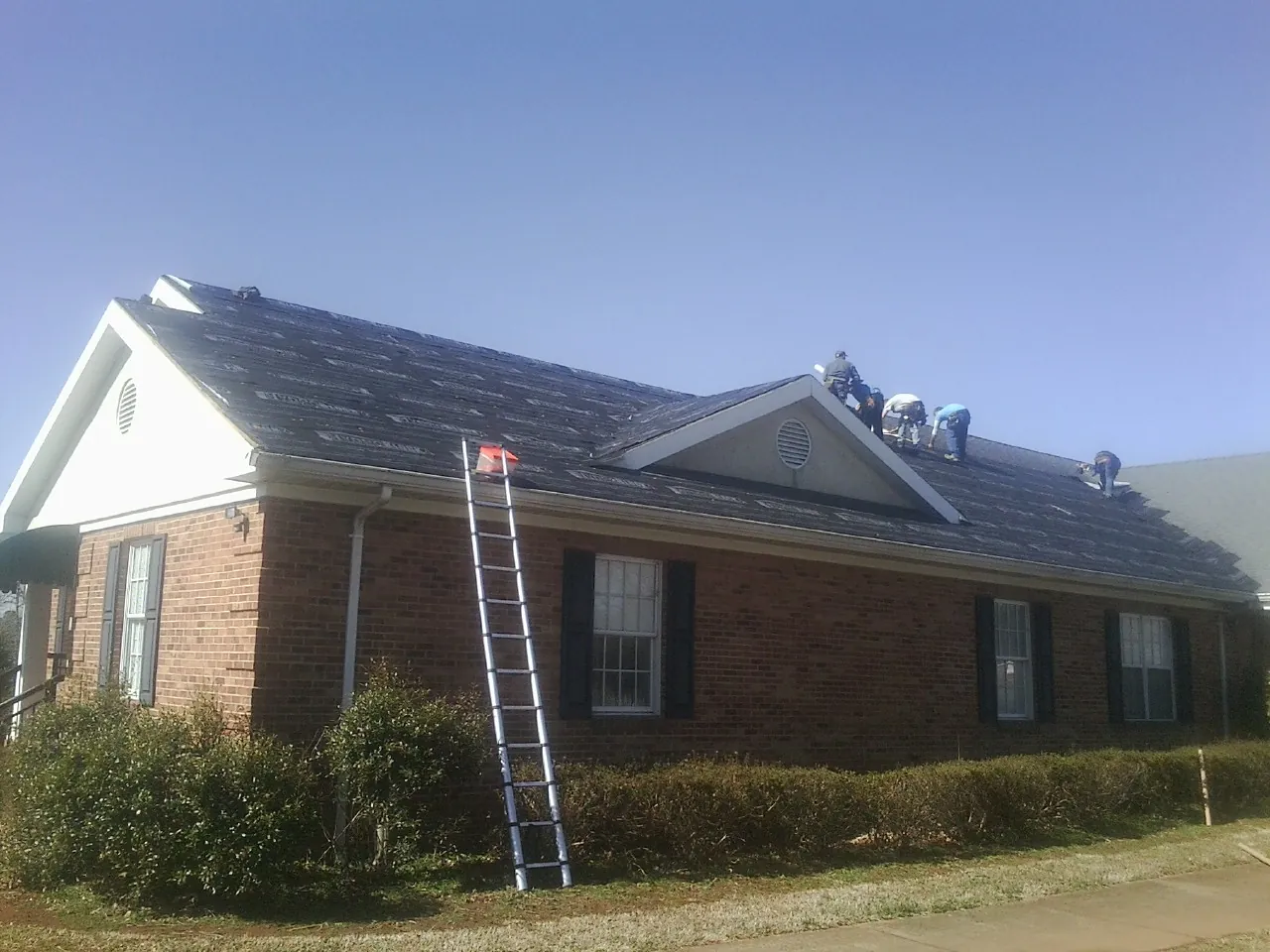 Crew tearing shingles off a brick ranch roof with a ladder set — Emergency Roof Repair work by our crew in Hadlyme