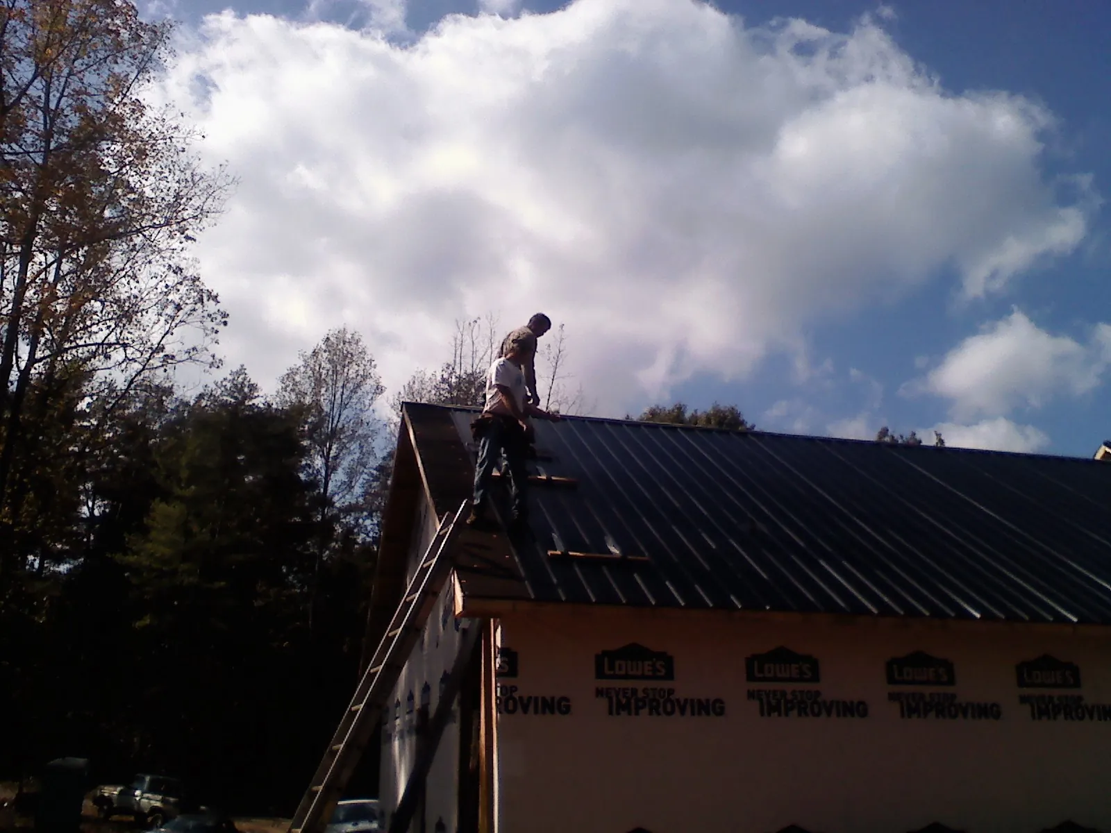 Roofer fastening dark metal panels high against a cloudy sky, from a Roof Inspection job in Hadlyme