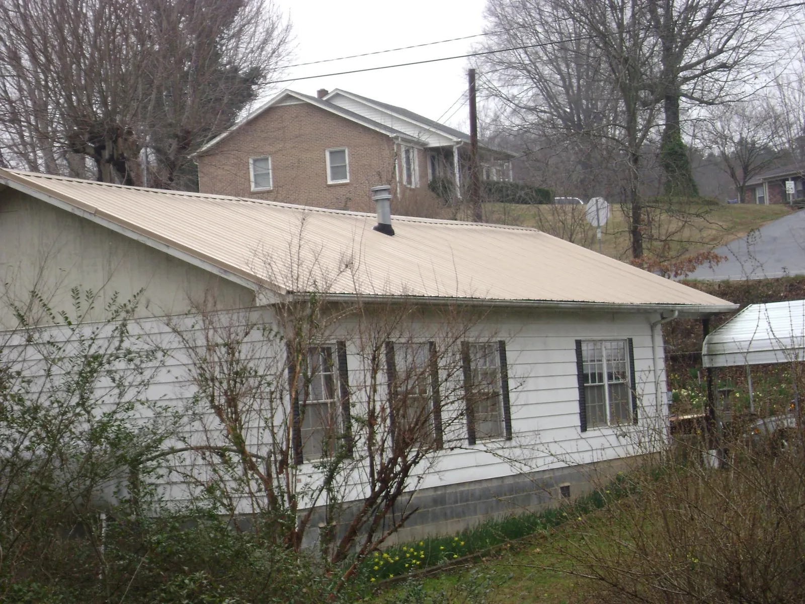 Tan metal roof on a white sided house set into a hillside — Commercial Roofing by Roofing Brothers in Hadlyme